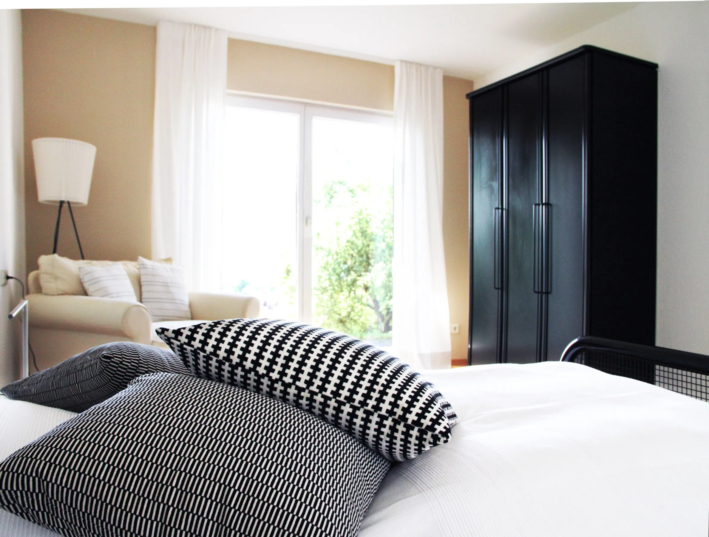 Schlafraum des Apartments mit Doppelbett, schwarzem Kleiderschrank und hellem Sessel am Fenster