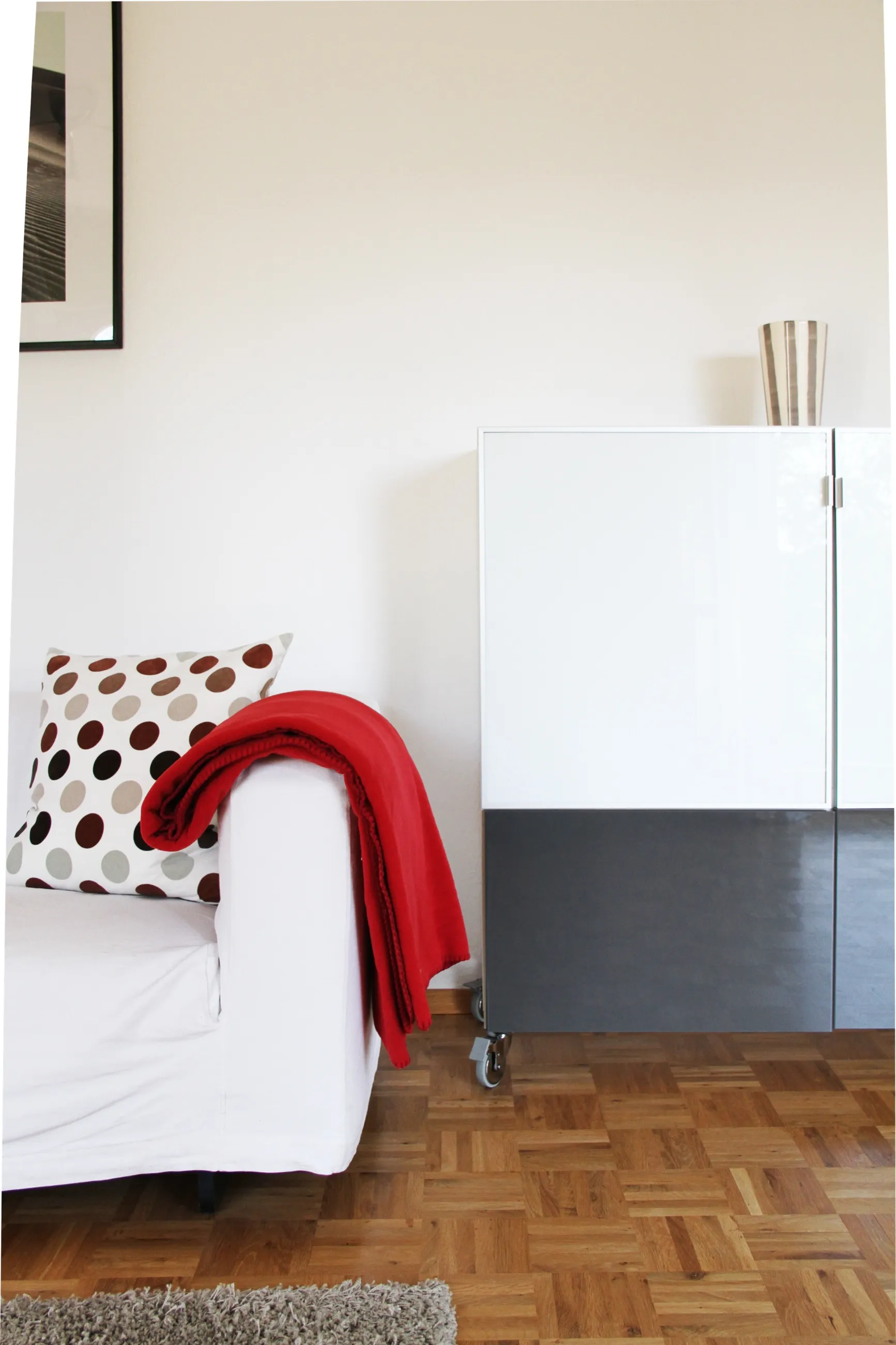 Sofa mit roter Decke und gepunkteten Kissen vor einem weißen Sideboard