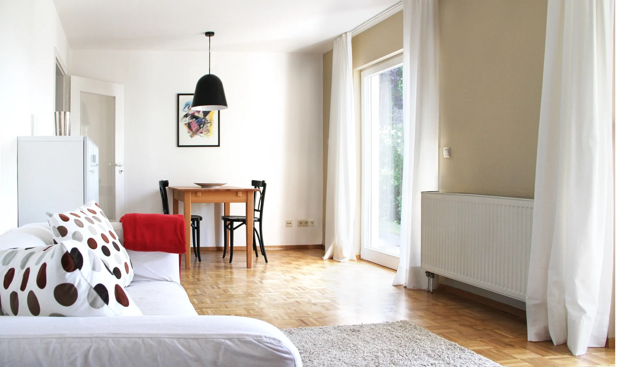 Möbliertes Apartment in Rosengarten-Westheim bei Schwäbisch Hall: Wohnbereich mit hellem Sofa, Esstisch unter schwarzer Pendelleuchte, bodentiefe Fenster und Parkett